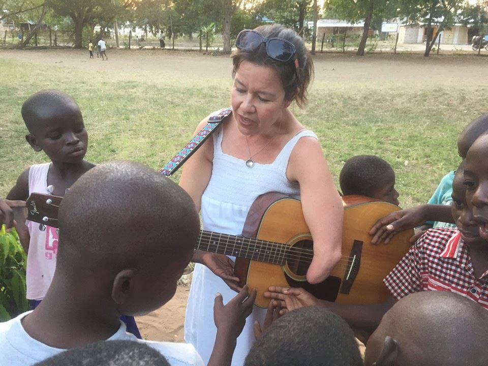 Cynthia Bauer plays her guitar, surrounded by children. Image credit: Britta Magnuson
