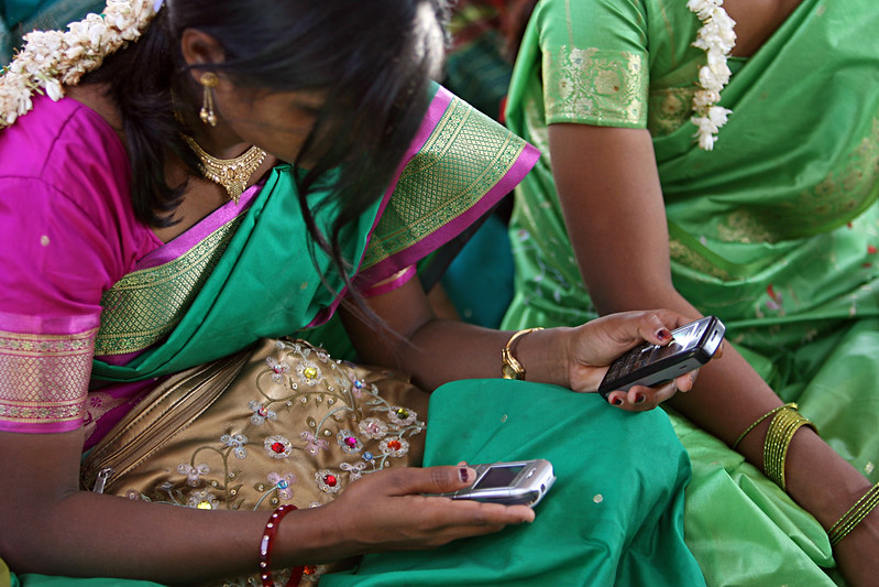 Young women look at their cellphone. Photo Credit: Credit: Simone D. McCourtie/World Bank