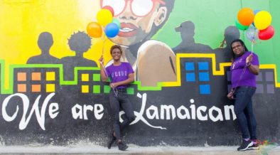 Dalawang Jamaican na nakatayo sa harap ng wall mural na may nakasulat na "We are Jamaican". JFLAG Pride, 2020 © JFLAG