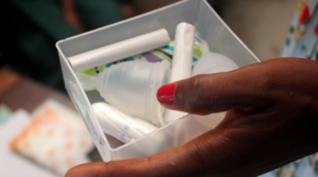 A hand holding a see-through container with menstrual health supplies—tampons and menstrual cups