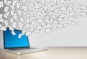 Um laptop com uma tela azul. Dezenas de envelopes ilustrados se espalham dele. 