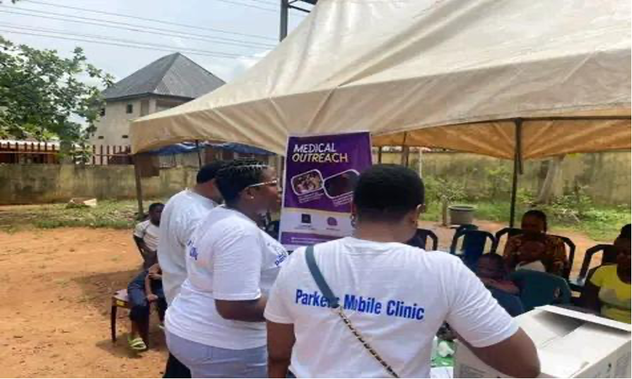 Three Parkers Mobile Clinic employees at an information session. Their backs are to the camera as they approach a pavilion. They wear Parkers Mobile Clinic t-shirts.