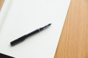 A black pen sits atop an empty notebook with grid paper.