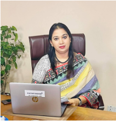 Image of Dr. Farhana Huq sitting at a desk, facing the camera. She works on a laptop computer.