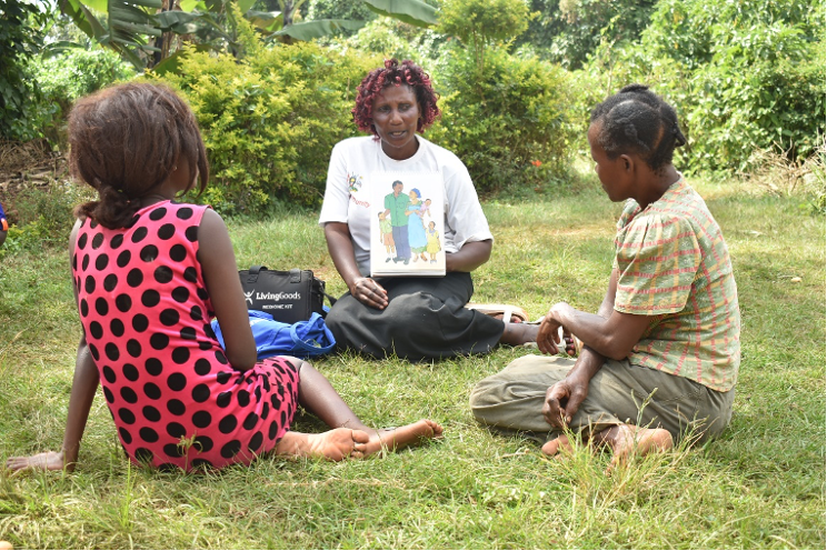 Community health worker Betty speaks with a mother (Florence) and daughter (Rachael) about different family planning methods. They sit in soft green grass, surrounded by lush shrubbery.