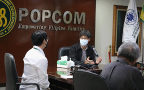Pekerja POPCOM yang memakai topeng duduk di sekeliling meja persidangan untuk membincangkan mandat mereka pada mesyuarat dalaman. Kredit gambar: POPCOM