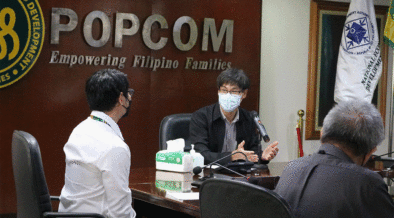 Los empleados de POPCOM con máscaras se sientan alrededor de una mesa de conferencias para discutir su mandato en una reunión interna. Credito de imagen: popcom