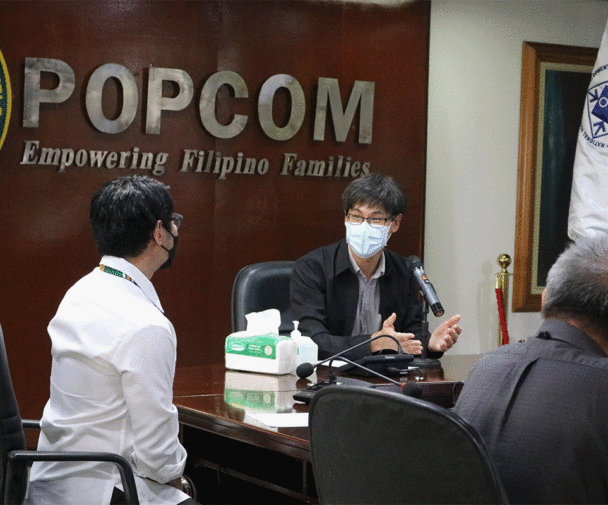 POPCOM employees wearing masks sit around a conference table to discuss their mandate at an internal meeting. Image credit: POPCOM