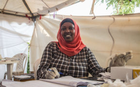 Seorang pekerja kesihatan wanita duduk di meja yang menganjurkan penjualan produk penjagaan kesihatan sebagai sebahagian daripada program jangkauan komuniti di Rwanda.
