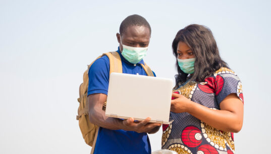 Man and woman with facemasks looking at a laptop computer.
