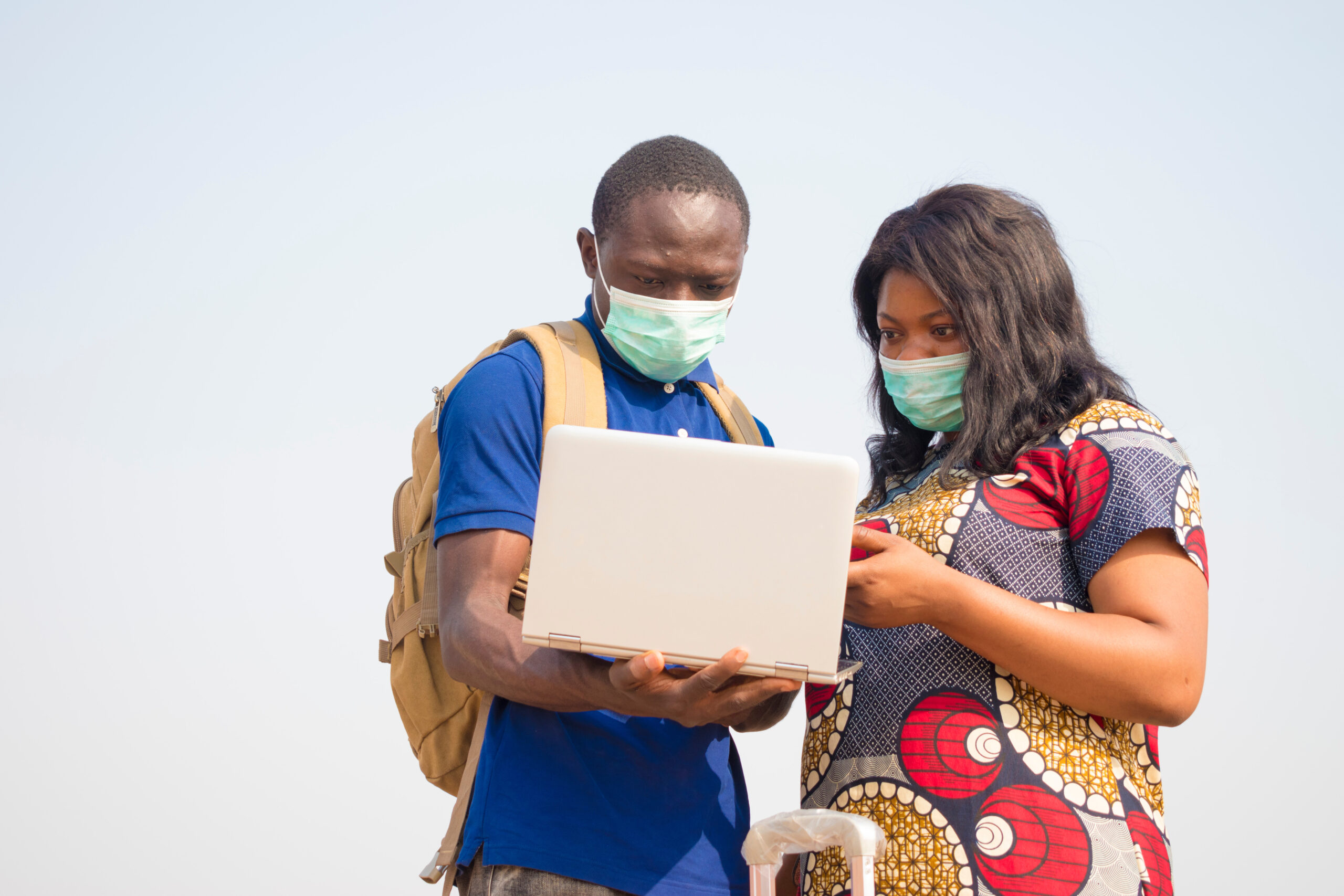 Man and woman with facemasks looking at a laptop computer.