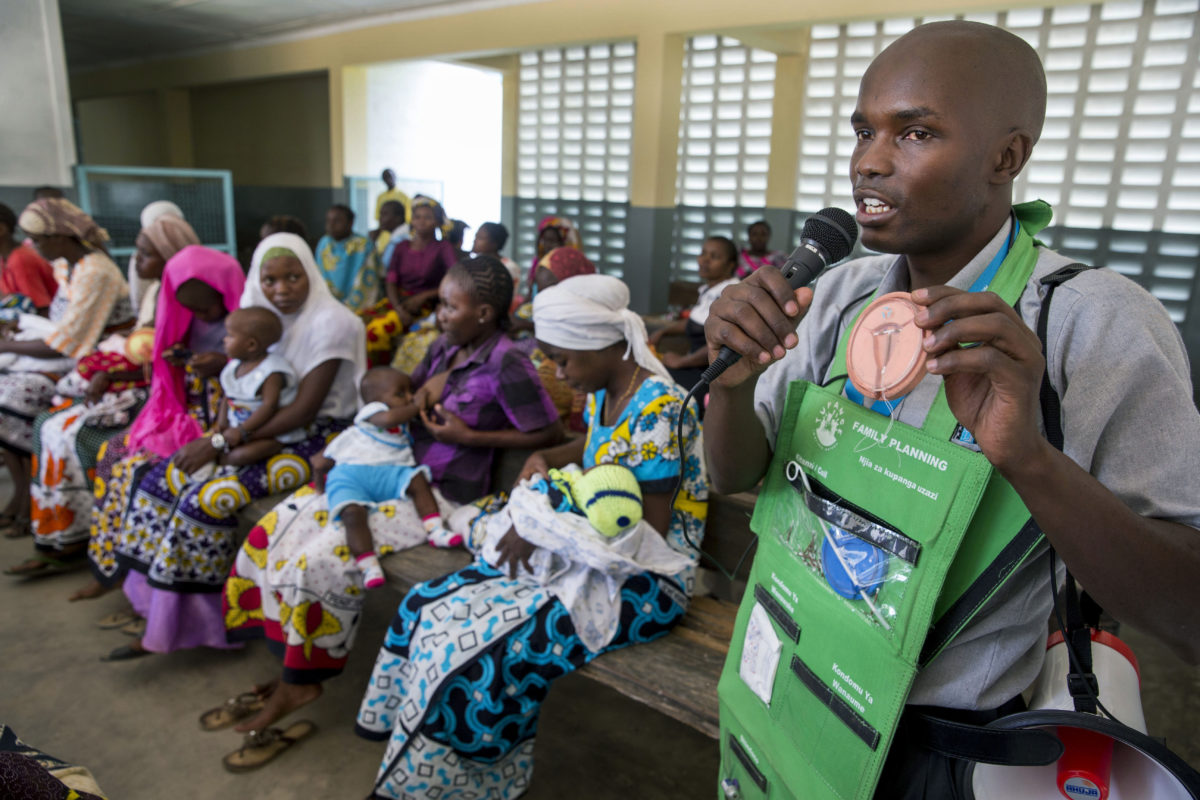 Kenyan community health worker speaking into a microphone to a group of women about contraceptive options at a hospital.