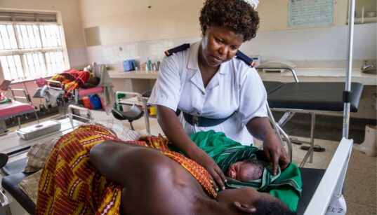 Nurse caring for mother and newborn in hospital bed.