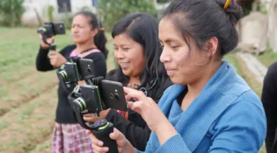 Three women standing in a field recording with smartphones on gimbals