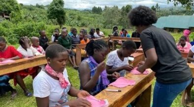 Adolescent girls sit at wooden desks with menstrual pad materials.